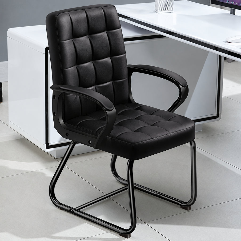 Black faux leather office chair with tufted padding, armrests, and a cantilevered metal frame, shown in a modern office setting
