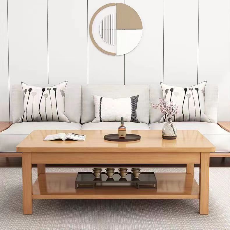 A modern light oak wood rectangular coffee table with two shelves, styled in a minimalist living room setting with a white sofa, decorative pillows, and a wall mirror behind it.
