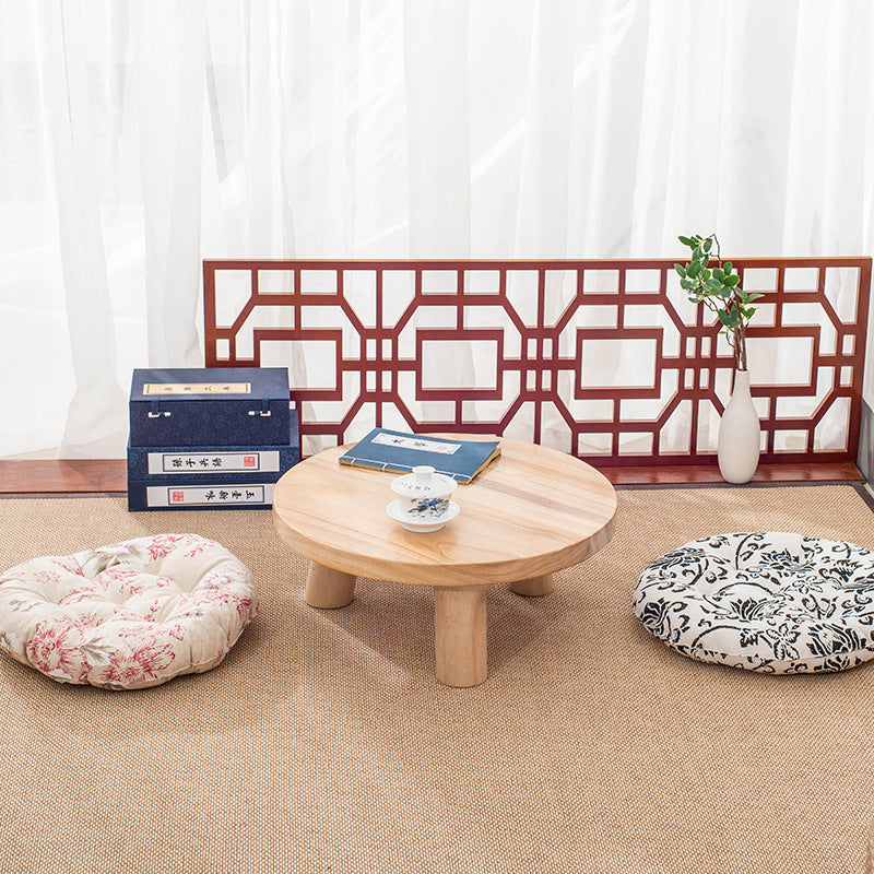 Natural Round Timber Coffee Table with cushions on a beige floor against a white curtain backdrop