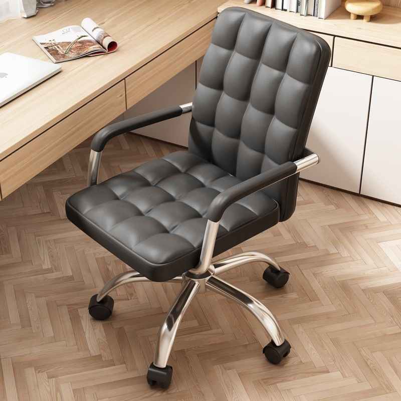 A black faux leather office chair with a tufted grid pattern on the seat and backrest, supported by a chrome five-star base with black casters, shown in a home office setting next to a wooden desk.