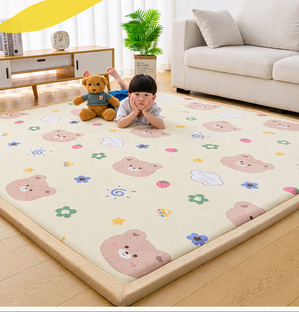 A children's floor mat with a beige base and a playful cartoon print of teddy bears, stars, and flowers, shown in a cozy living room setting with a child lying on it. The image includes promotional text at the top.