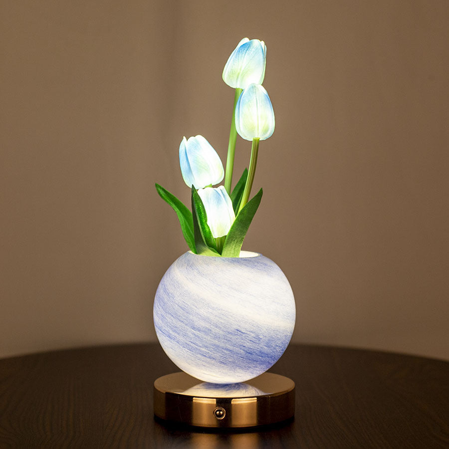 Decorative lamp with glowing tulip-shaped lights in a white and blue marbled vase on a wooden surface.