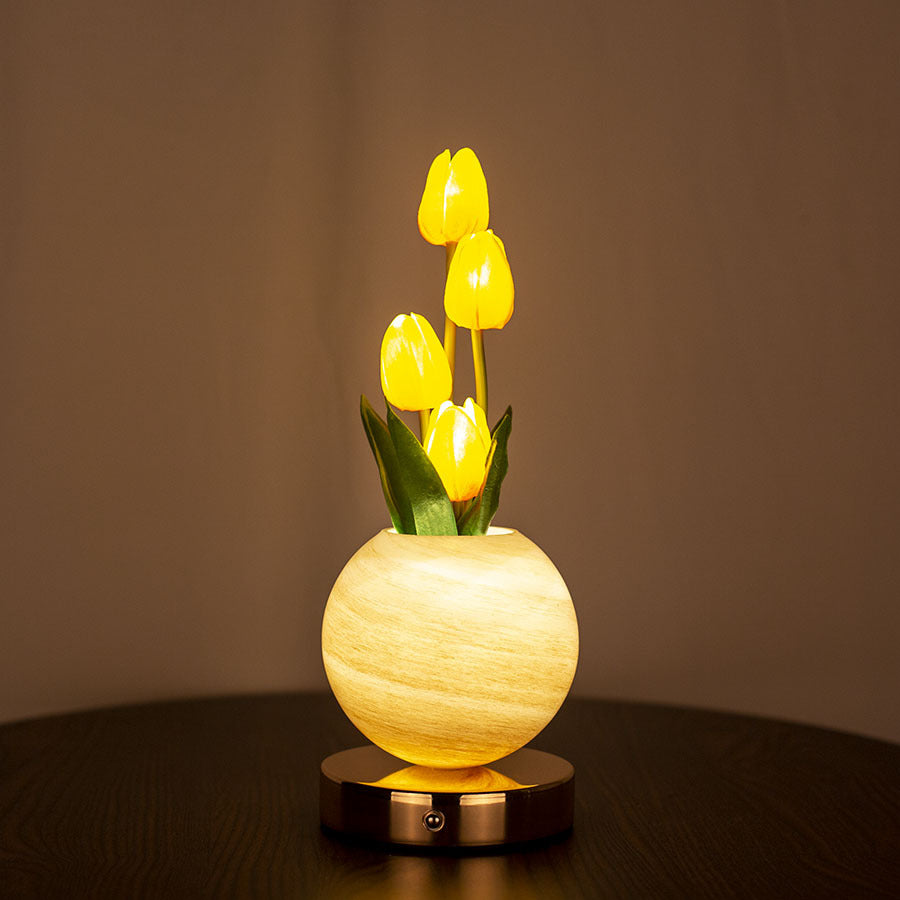 Decorative lamp with yellow tulips in a round, light-colored base on a dark surface.