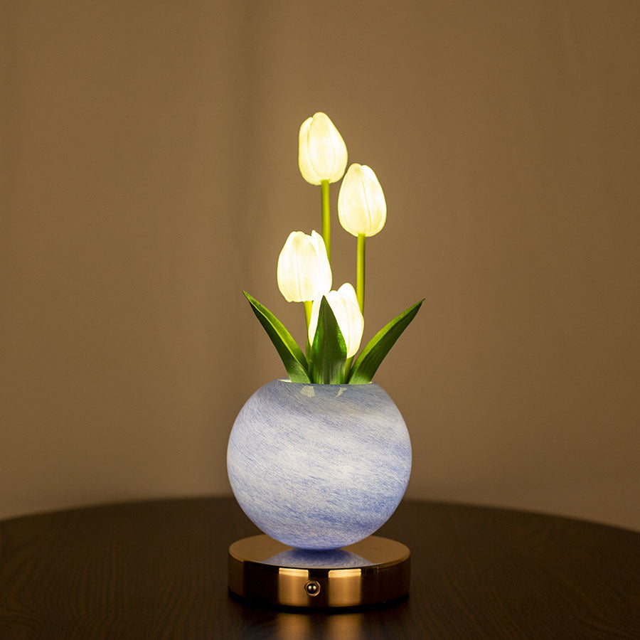 Decorative lamp with illuminated tulips in a marble-like vase on a wooden surface.