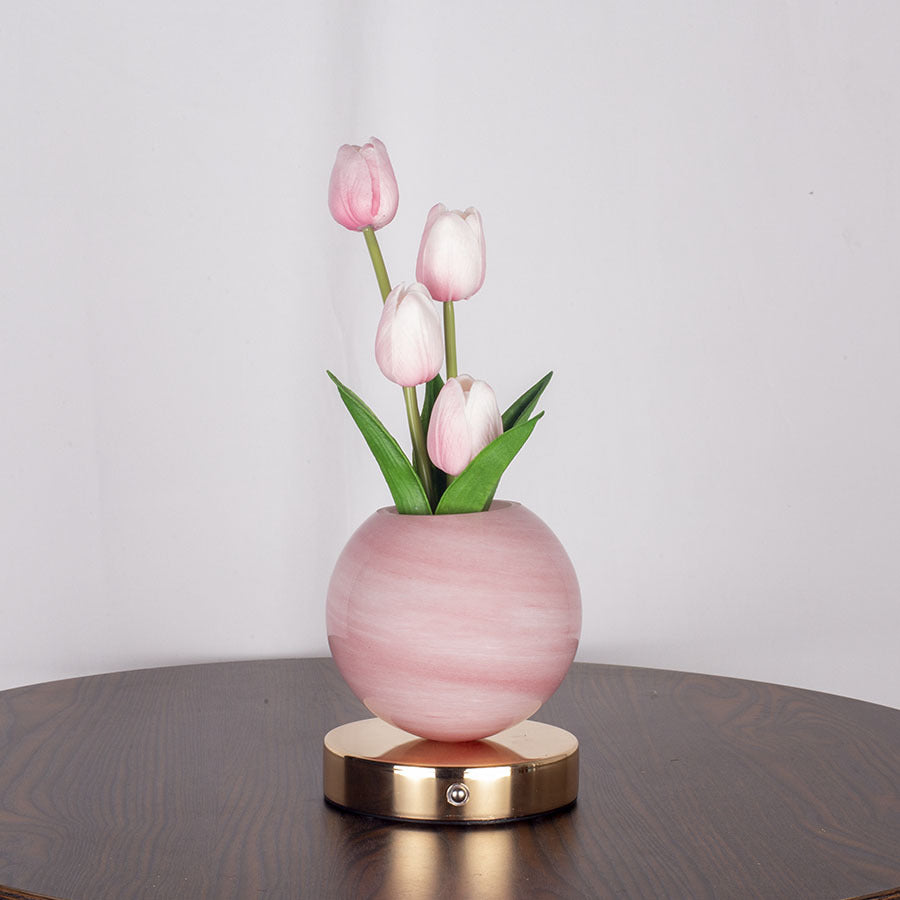 Pink vase with tulips on a wooden surface against a white wall