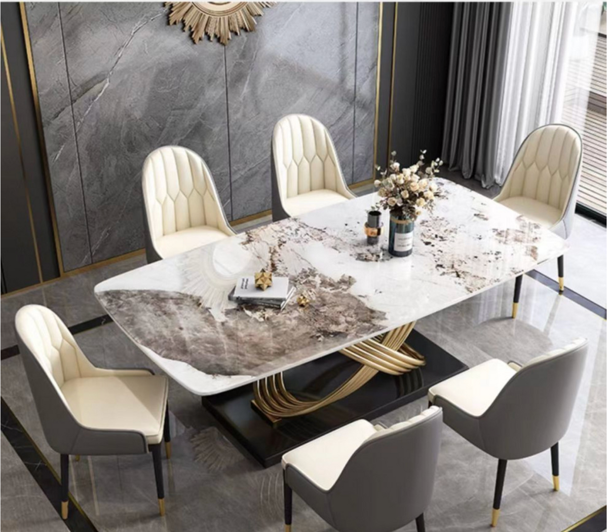 A modern rectangular dining table with a white and gray marbled stone top and a gold curved metal base, surrounded by six upholstered chairs in cream and gray, set in a luxury dining room.
