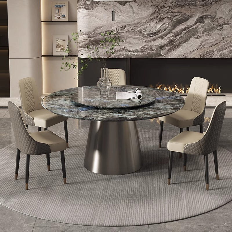 A round dark marble dining table with a brushed metal pedestal base, surrounded by four upholstered dining chairs in a modern dining room setting.