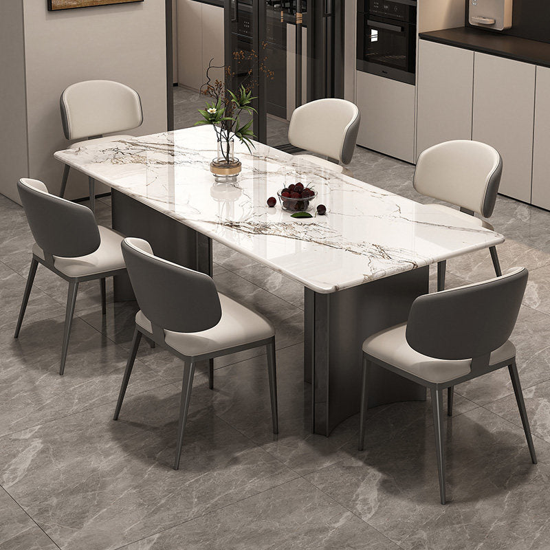 A modern rectangular dining table with a white marble-look top and dark gray base, surrounded by six gray upholstered dining chairs with light gray backs, shown in a contemporary dining room setting.