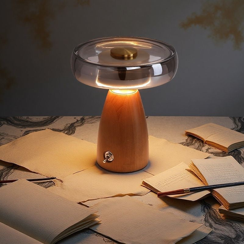 Table lamp with a wooden base and glass shade on a table with books and papers.