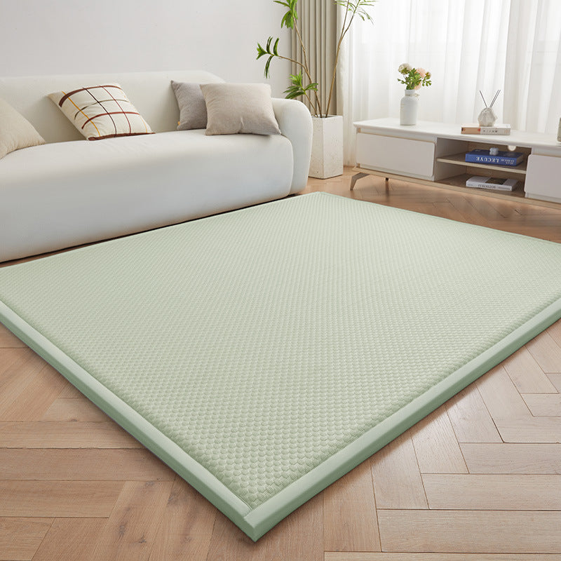 A light sage green textured floor mat or mattress topper laid out on a light wood herringbone floor in a bright, modern living room with a white sofa and white sideboard.