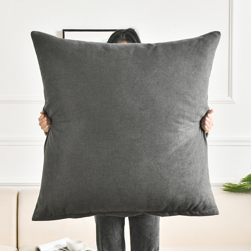 Person holding a large gray pillow against a white wall.