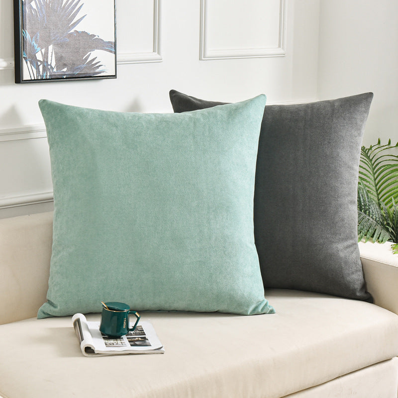 Two square throw pillows, one in mint green and one in dark gray, styled on a cream-colored sofa in a bright, modern living room setting.
