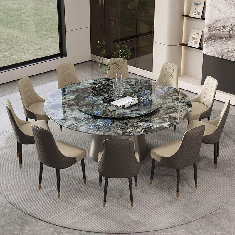 A round dining table with a dark marbled stone top and a central rotating platter, surrounded by eight upholstered dining chairs in beige and dark brown tones, set in a modern dining room.