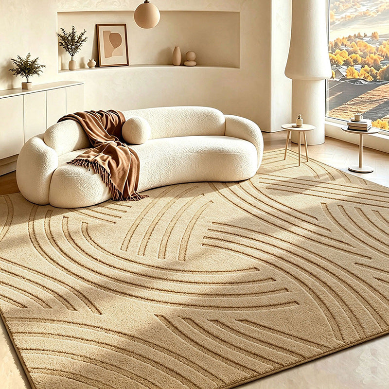 A large beige area rug with a raised wavy geometric pattern in a warm cream-toned living room. A curved cream boucle sofa with a brown throw blanket sits on the rug, and a large window on the right shows an outdoor landscape.