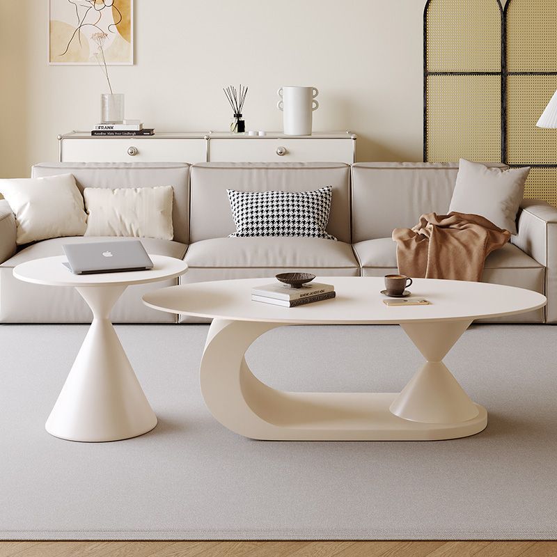 A modern living room scene featuring a round off-white coffee table and a matching side table with sculptural cone-shaped legs, styled on a light rug in front of a beige sofa.