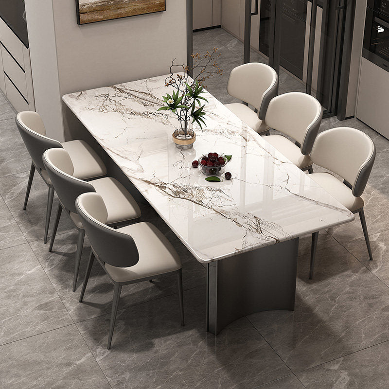 A modern rectangular dining table with a white marble-look top and dark gray curved base, surrounded by six upholstered dining chairs in a neutral-toned dining room.